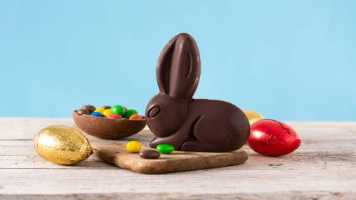 Coelho de chocolate com ovos coloridos sobre uma mesa de madeira com fundo azul