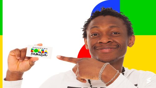 Homem sorridente de pele escura apontando para um cartão do Programa Bolsa Família sobre fundo colorido