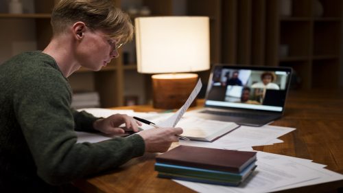 Jovem estudando em sala virtual com documentos e computador à noite