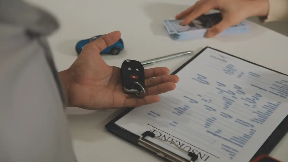 Maos com chave de veiculo e documentos sobre uma mesa.